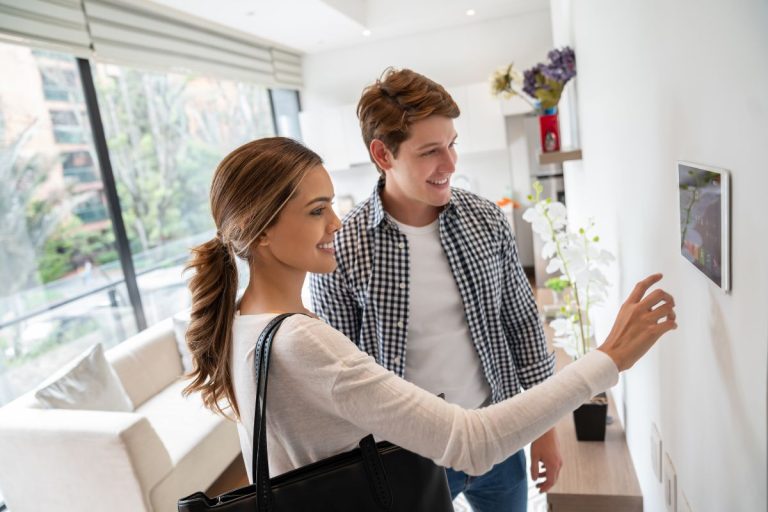 A man and woman are engaged in conversation while observing a smart home device in their living room.