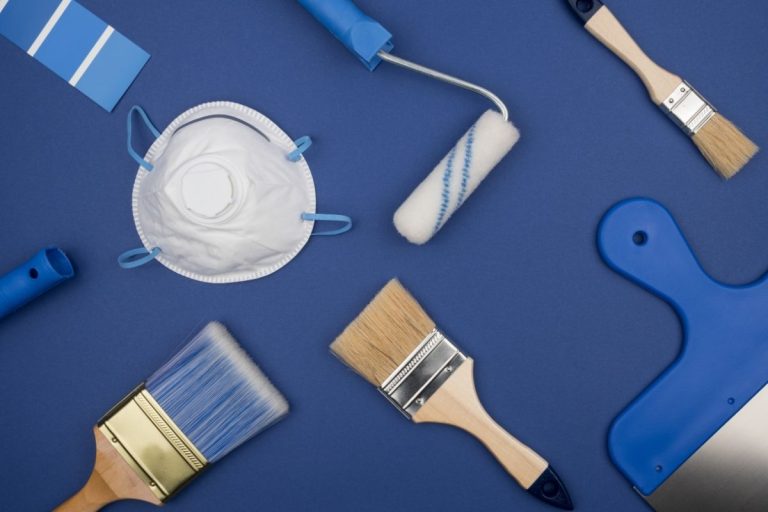 A collection of paint brushes, rollers, cans, and a mask arranged on a surface, ready for a painting project.