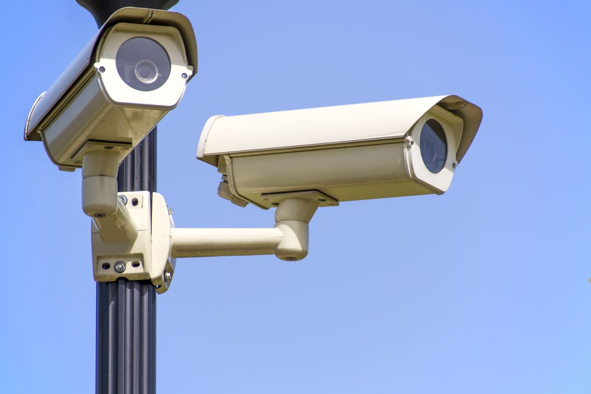 Two surveillance cameras mounted on a lamp post against a clear blue sky, monitoring the surrounding area.